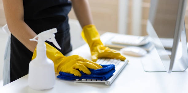 Profesional de limpieza con guantes limpiando ordenador en oficina en Madrid para mantener un espacio de trabajo higiénico y eficiente